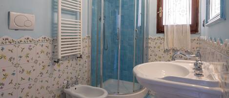 A bathroom with a shower, toilet, bidet, and sink.