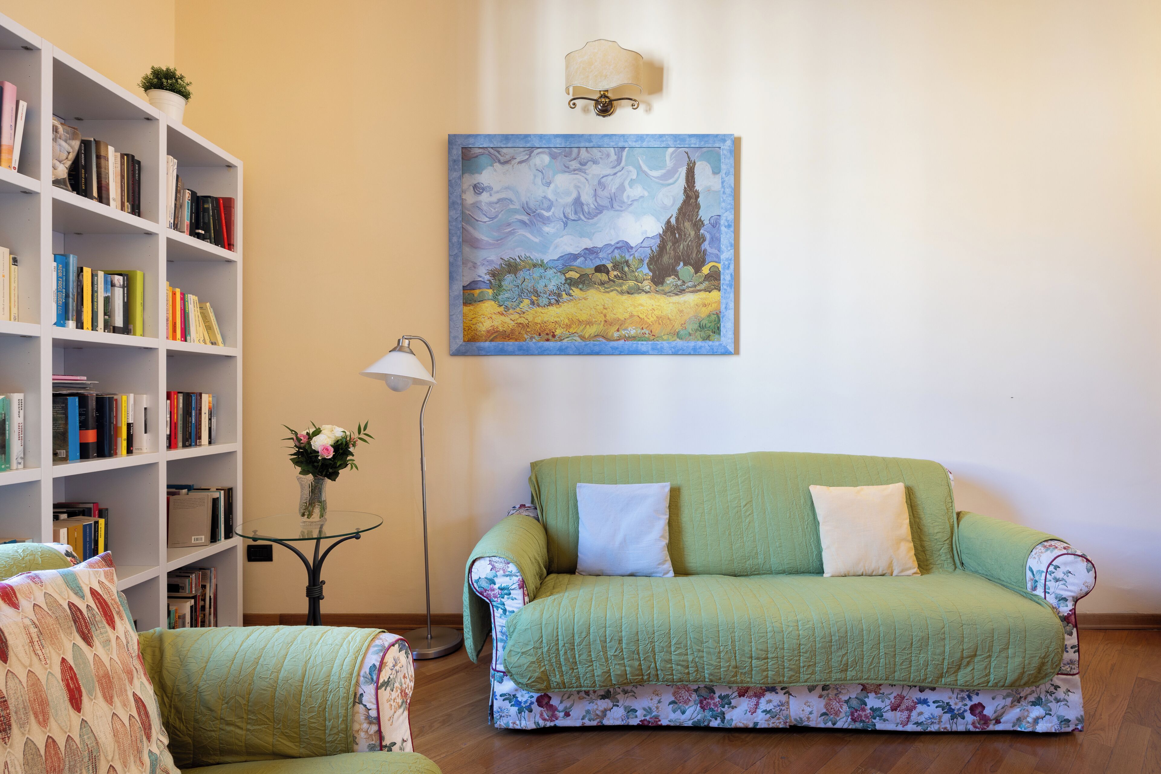 A living room with a green sofa, a bookshelf, and a painting of a landscape.