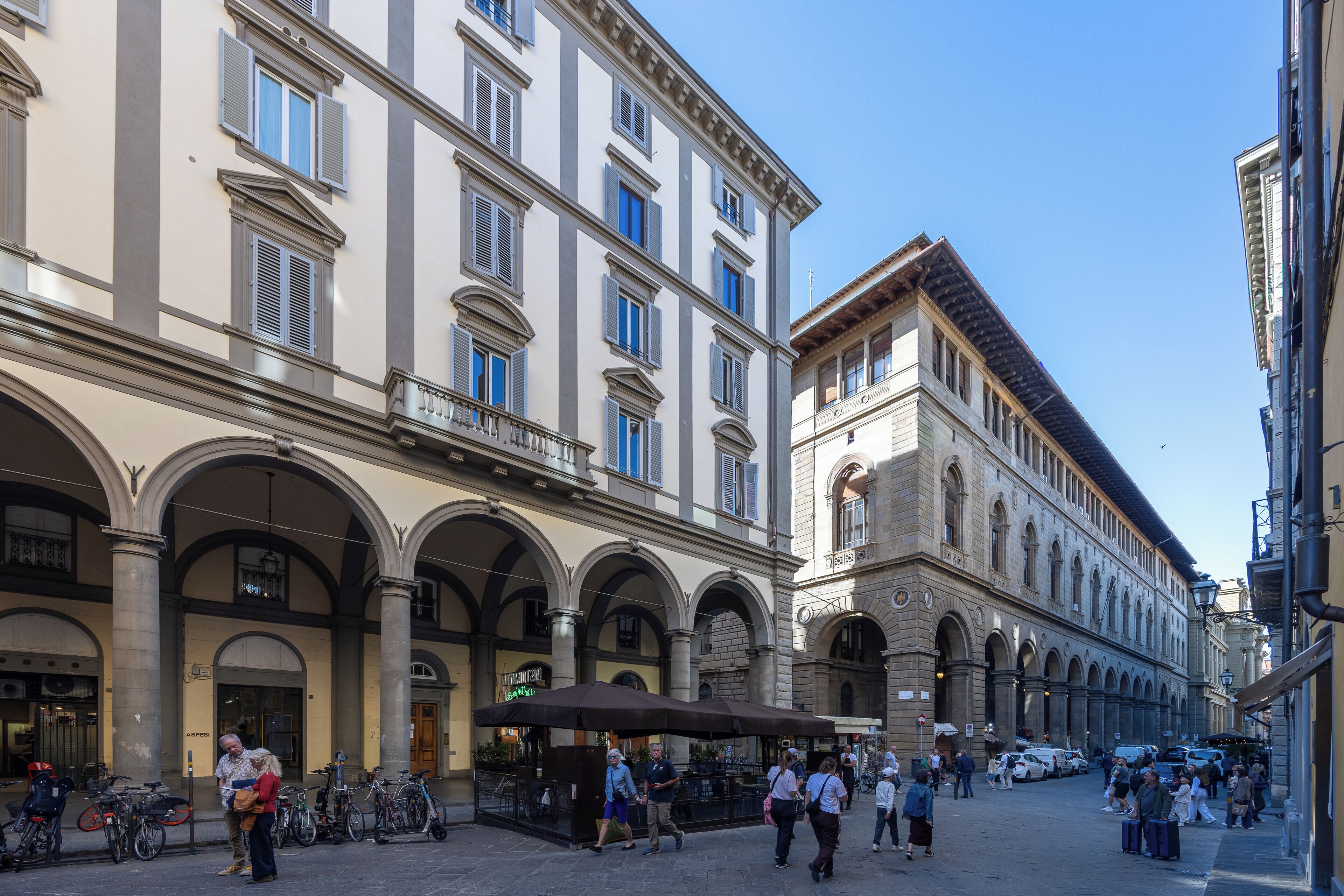 A historic street with classical architecture, including arches and columns, and a café with outdoor seating.