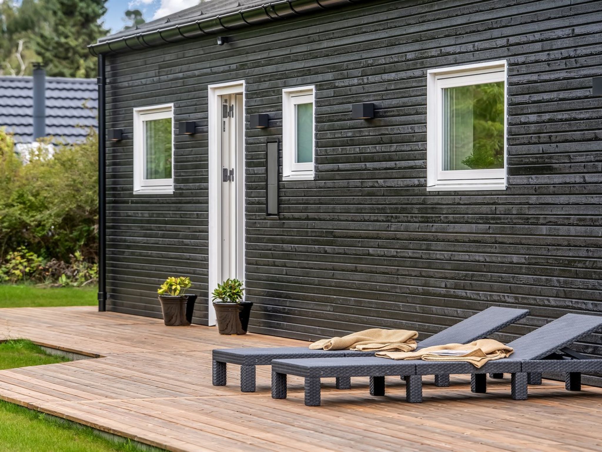 A modern house with a dark exterior, a wooden deck, and outdoor seating.