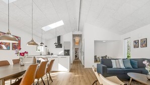 Eine moderne Küche mit Kochinsel, Essbereich mit Stühlen und ein Wohnzimmer mit Sofa und Couchtisch.