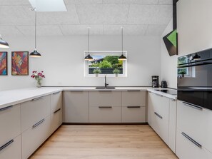 Et moderne køkken med en central ø, hængende lamper og udsigt gennem et vindue.