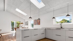 Eine moderne Küche mit weißen Schränken, einer großen Kochinsel, Pendelleuchten und Blick ins Freie.
