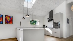 Eine moderne Küche mit einer zentralen Kochinsel, Pendelleuchten und Blick auf Grünfläche.