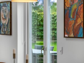 A room with a sliding glass door leading to an outdoor area, a table, and two paintings on the wall.