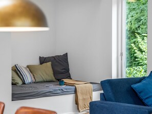 Hyggeligt opholdsområde med bænk, puder og et vindue med udsigt til grøn natur.