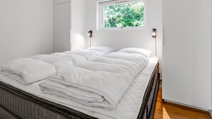 Ein modernes Schlafzimmer mit einem Bett, einem Fenster mit Blick auf Bäume und zwei Wandleuchten.