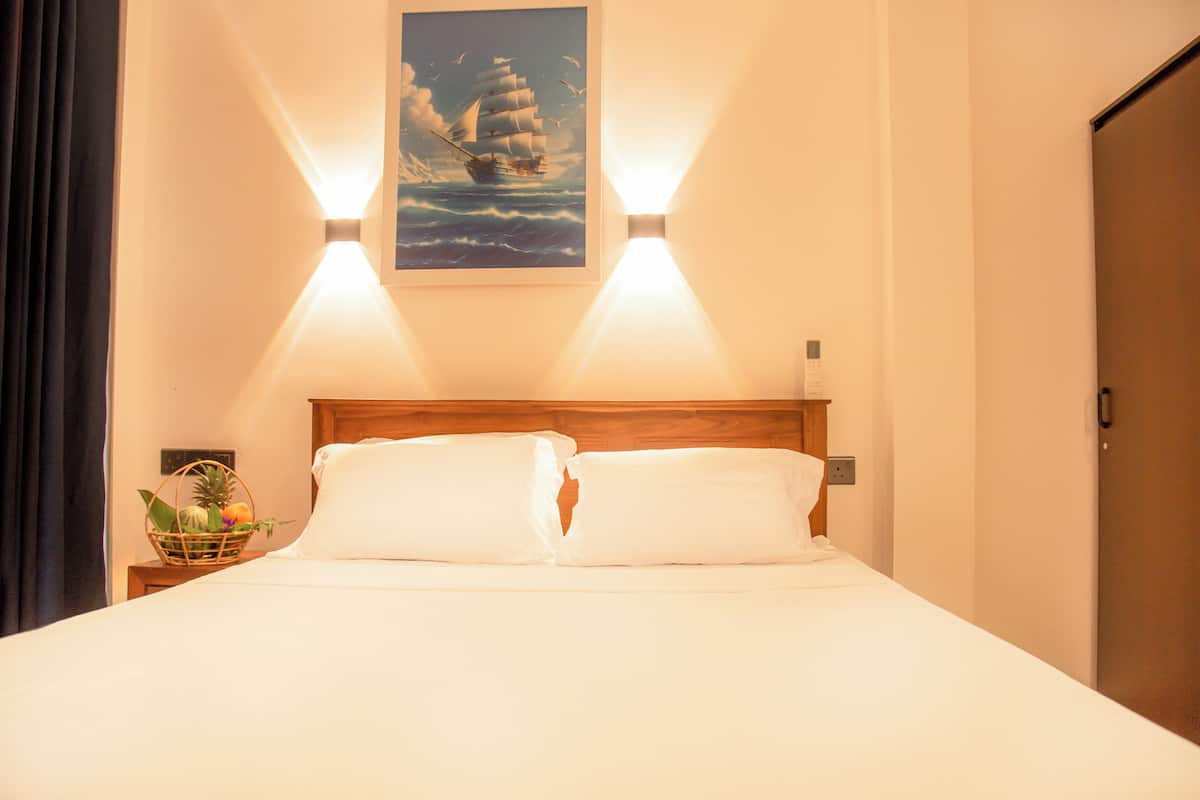 A neatly made bed with white linens, a wooden headboard, and a framed picture of a sailing ship on the wall.