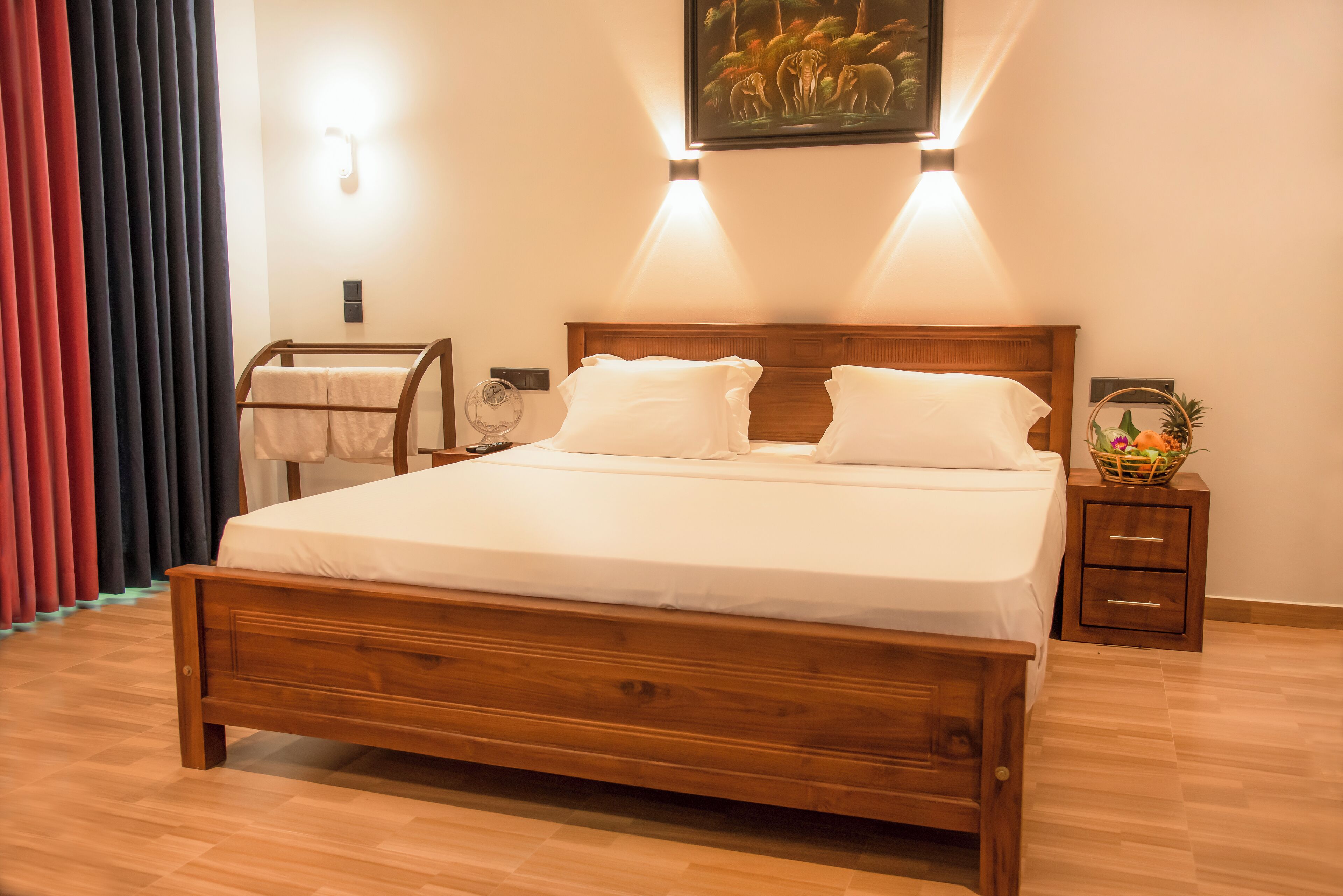 Una cama bien tendida con cabecera de madera, una mesita de noche con frutero y una lámpara de pared.