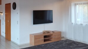 Amplia sala de estar con una televisión de pantalla plana grande, vigas de madera y una alfombra gris oscuro.