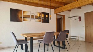Un comedor con una mesa de madera y cuatro sillas, un techo con vigas a la vista y una pared con arte abstracto.