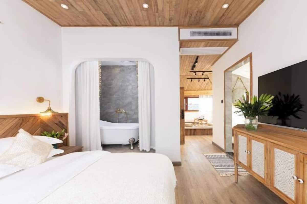 A modern bedroom with a large bed, a wooden ceiling, a built-in TV, and a walk-in closet.
