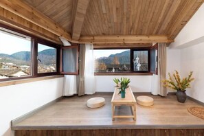 A room with a wooden ceiling, large windows with curtains, a wooden table, and a view of mountains. - Feng Mian Su She Guesthouse (Fenghuang)