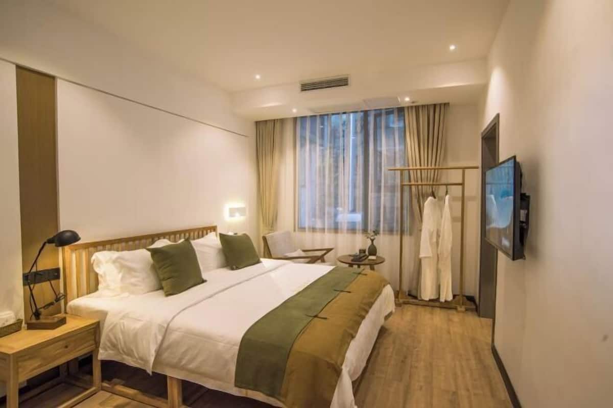 A hotel room with a bed, bedside table, lamp, chair, TV, and a window with curtains.
