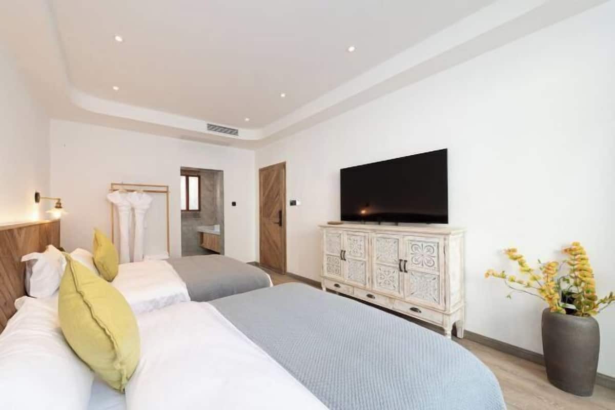 A hotel room with two beds, a television, a cabinet, and a vase with flowers.