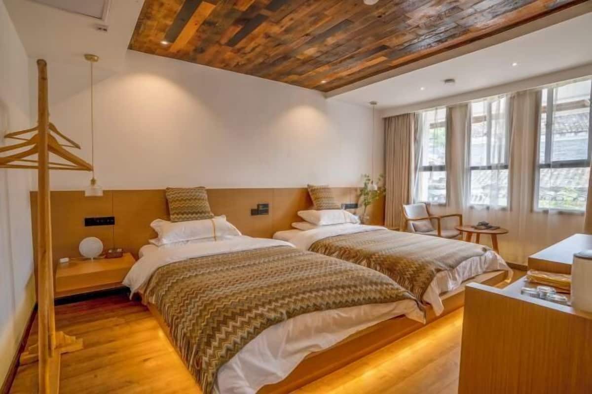 A hotel room with two beds, wooden flooring, a wooden ceiling, a desk, and a chair.
