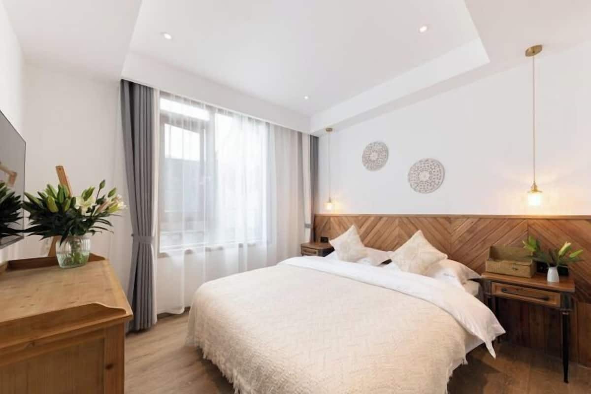A modern bedroom with a large bed, wooden headboard, bedside tables, and a large window with curtains.