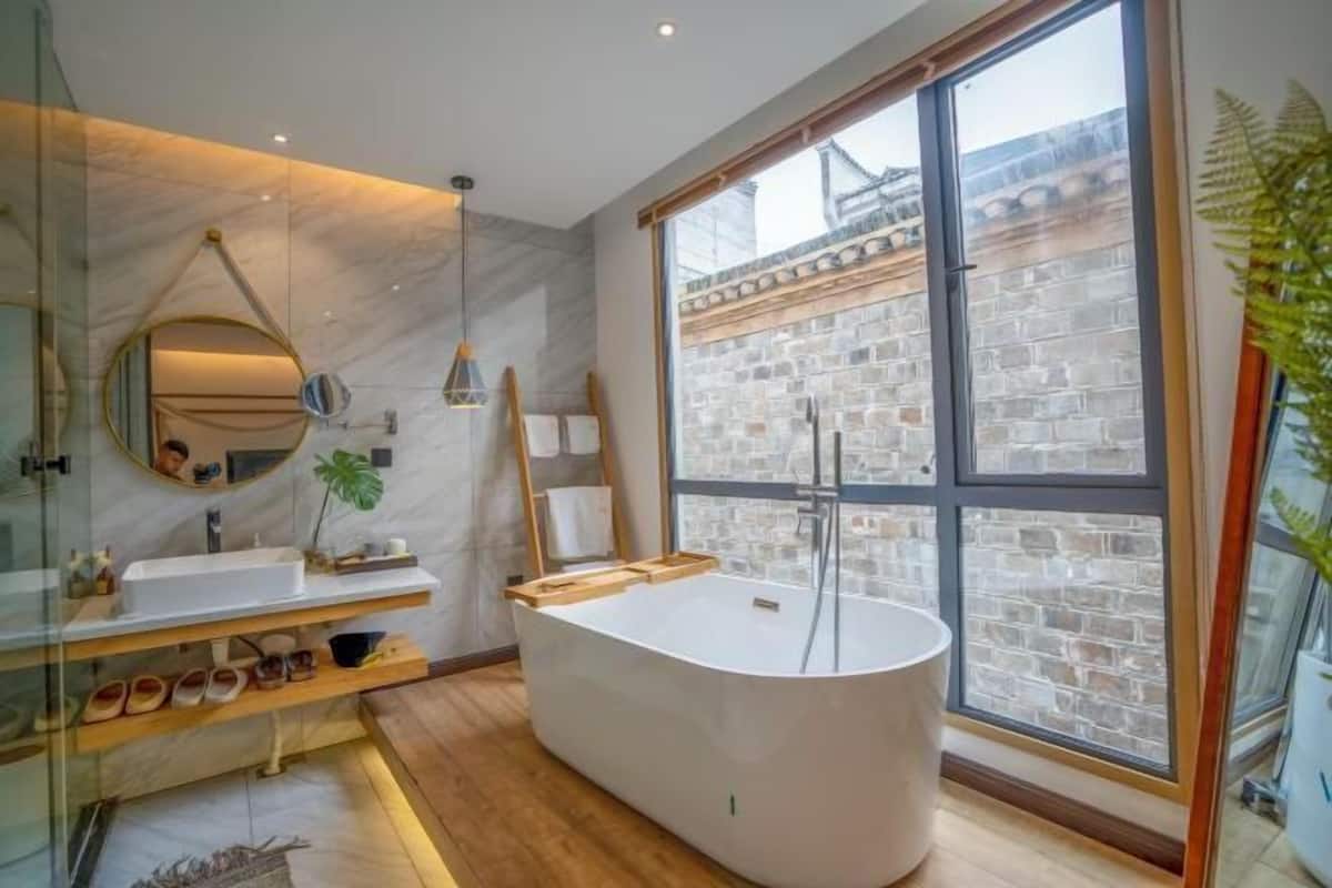 A modern bathroom with a freestanding bathtub, a large mirror, and a window with a view of a brick wall.