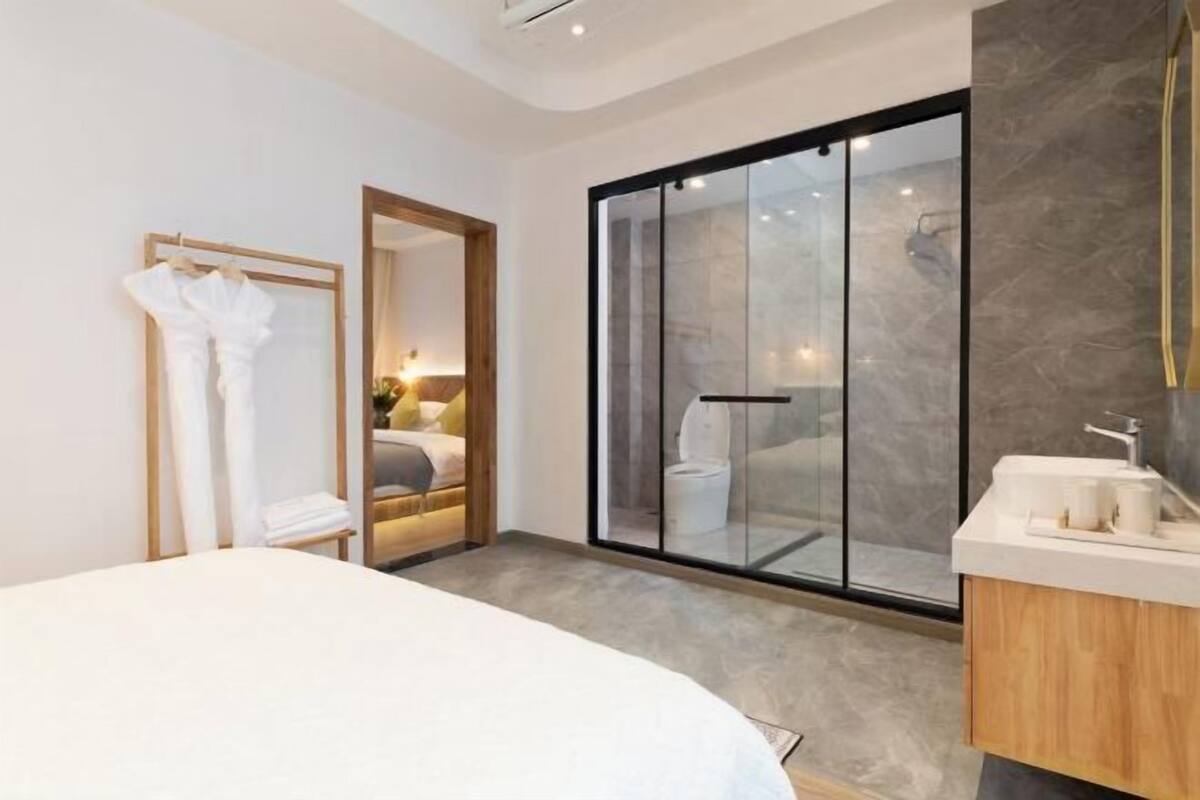 A modern hotel room with a large bed, a glass shower enclosure, a wooden vanity, and a mirror.