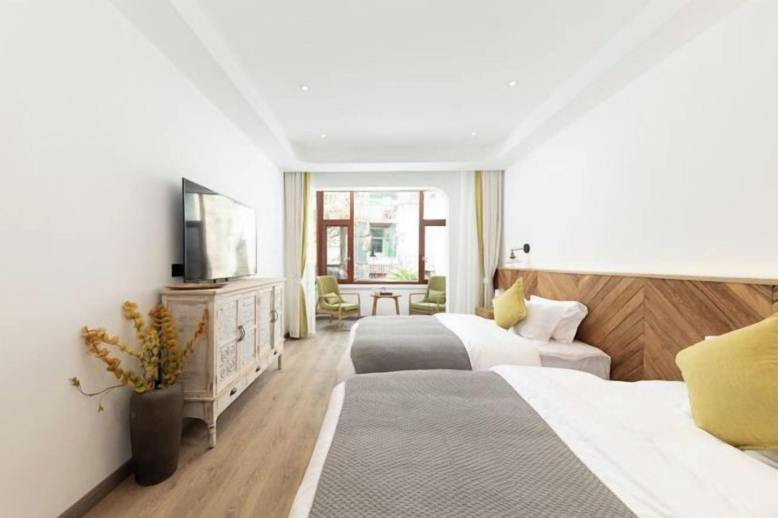 Une chambre d’hôtel avec deux lits, une tête de lit en bois, un téléviseur posé sur un meuble et une vue sur l’extérieur par une fenêtre.