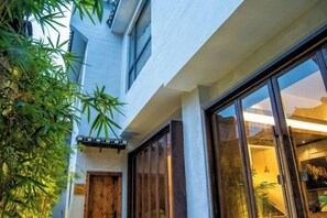 A building with a large glass door and windows, a wooden door, and a small balcony with plants. - Feng Mian Su She Guesthouse (Fenghuang)