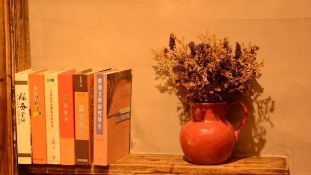 A bookshelf with books and a vase of dried flowers on a wooden shelf. - Hotel Baihui Inn (Zhangjiajie Pedestrian Street Dayong Ancient City Inn）) (Zhangjiajie)