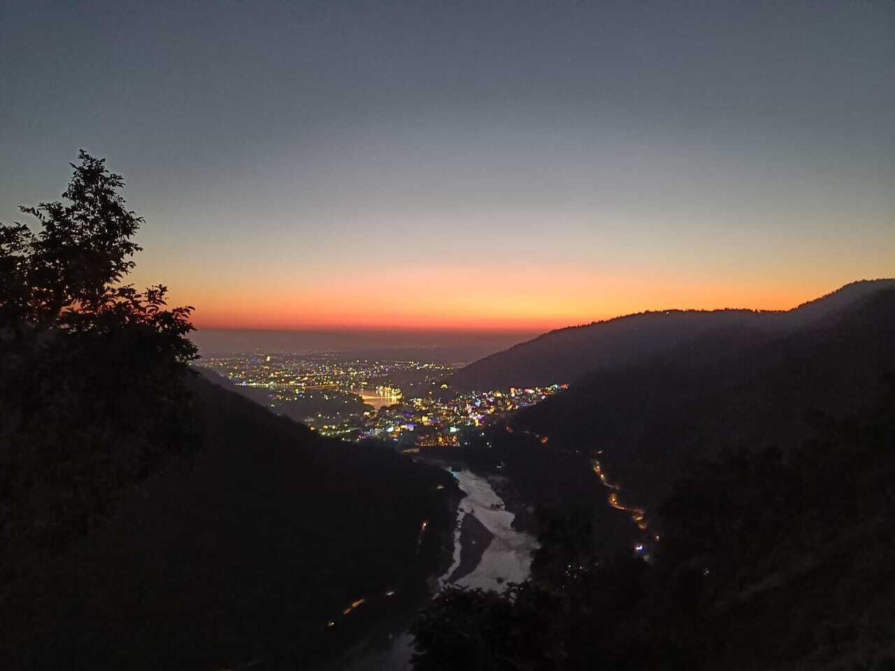 A nighttime view of a city with a river flowing through it, surrounded by hills.