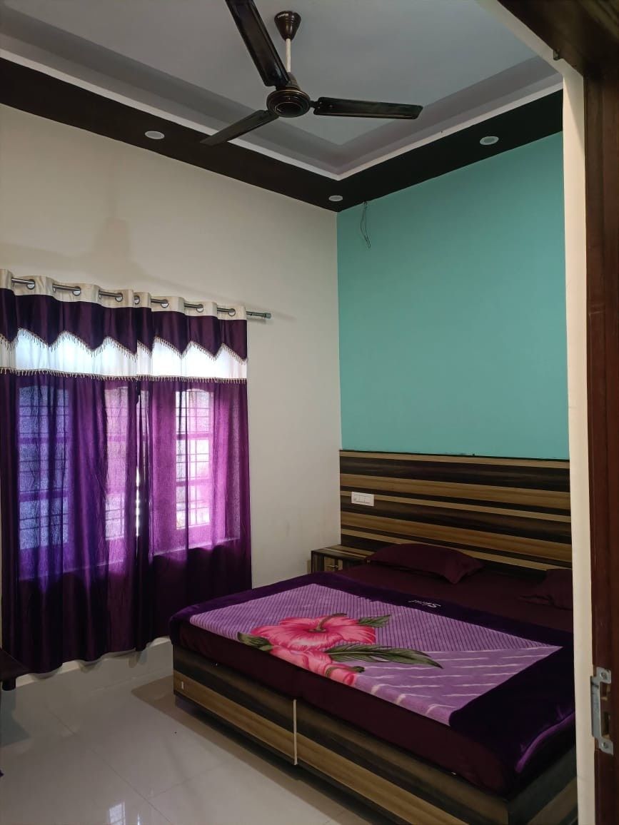 A bedroom with a bed, curtains, a ceiling fan, and a teal wall.