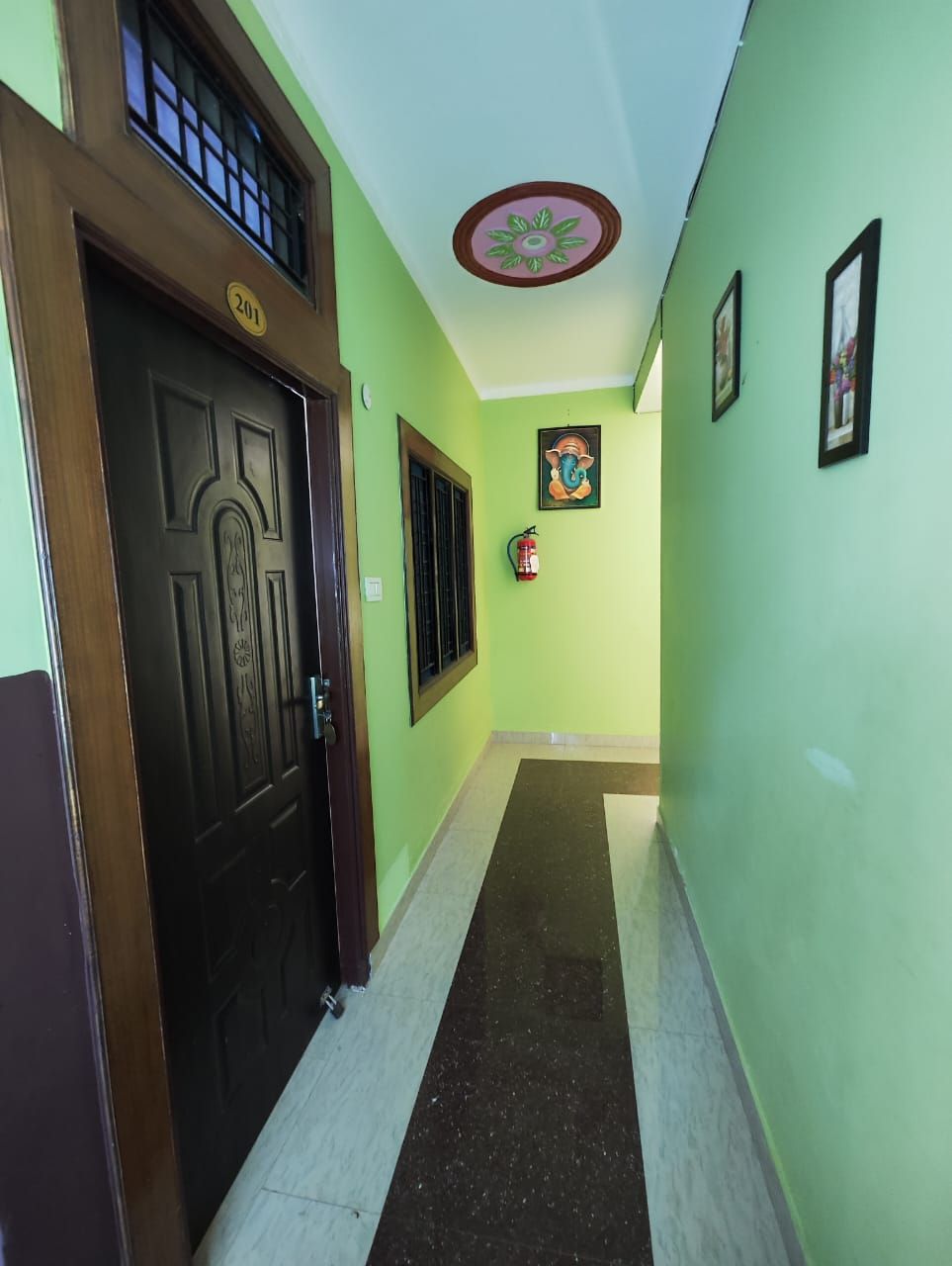 A hallway with a dark wooden door marked "201", a fire extinguisher, and framed pictures on the walls.
