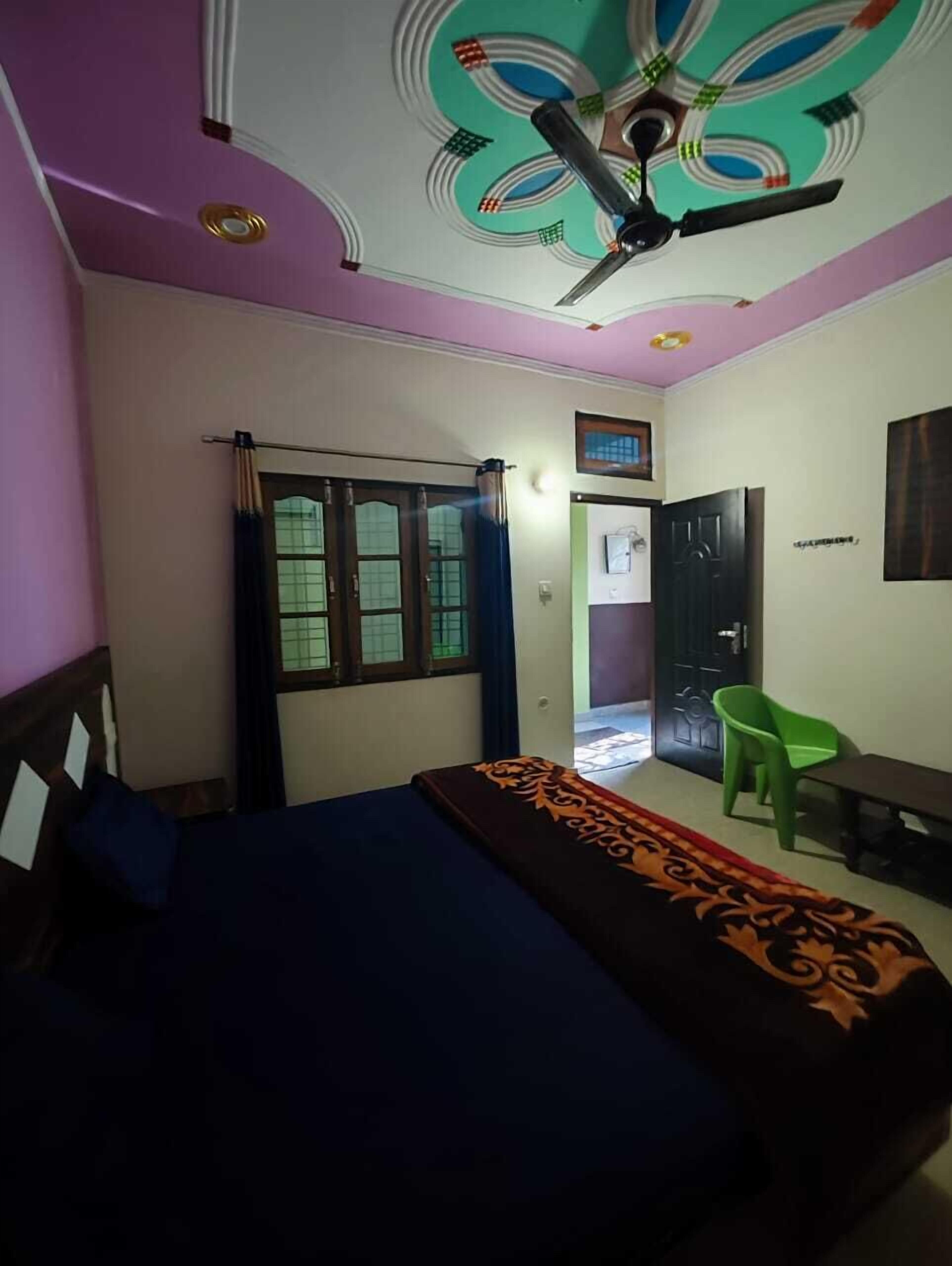 A bedroom with a bed, a ceiling fan, a window with curtains, a green chair, and a door.
