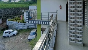 A modern building with a balcony, a stone pillar, and a view of a green landscape. - Nature villa Kyarki (Rishikesh)