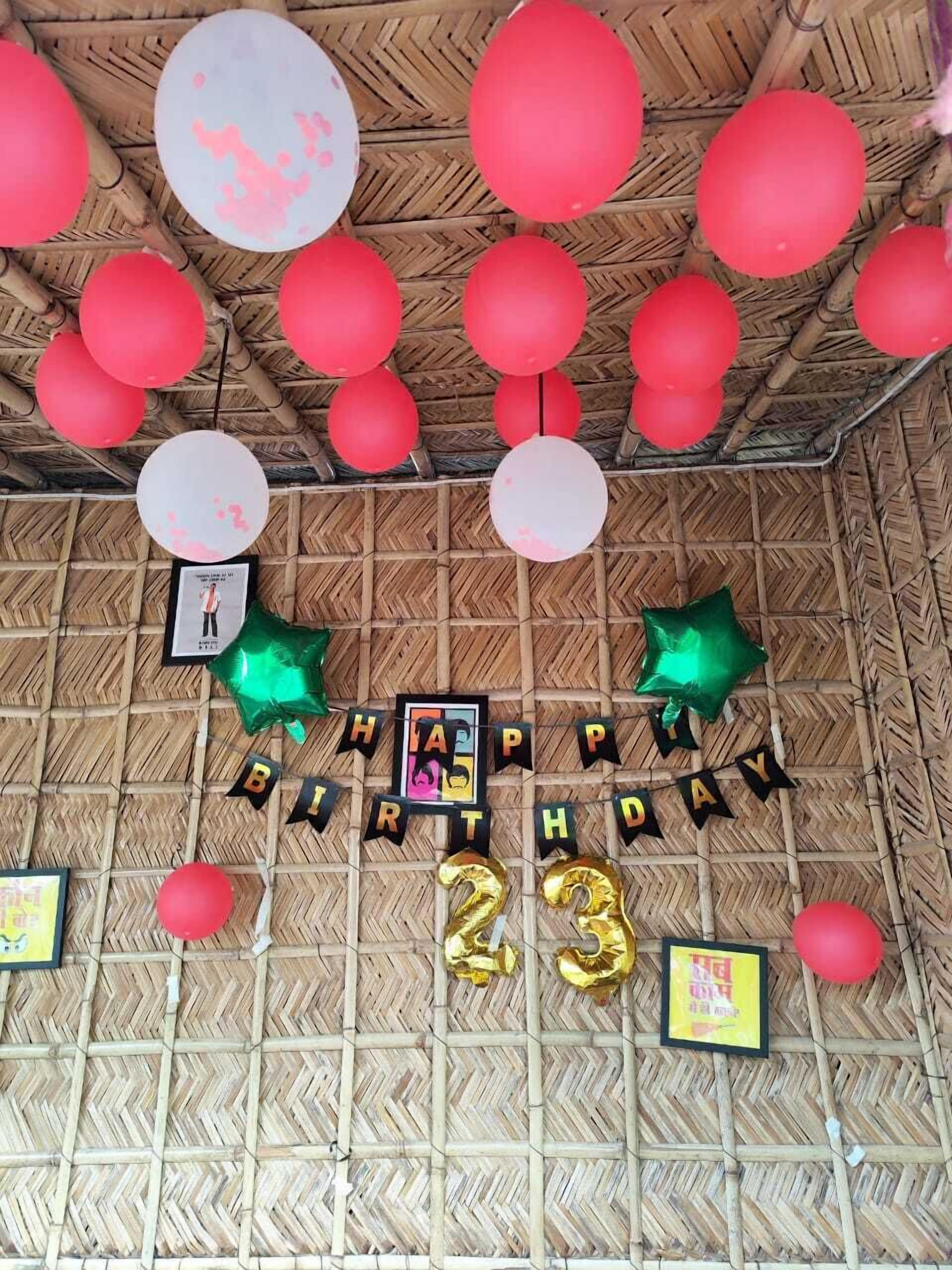 A bamboo ceiling with red and white balloons, a 'Happy Birthday 23' banner, and some framed pictures.