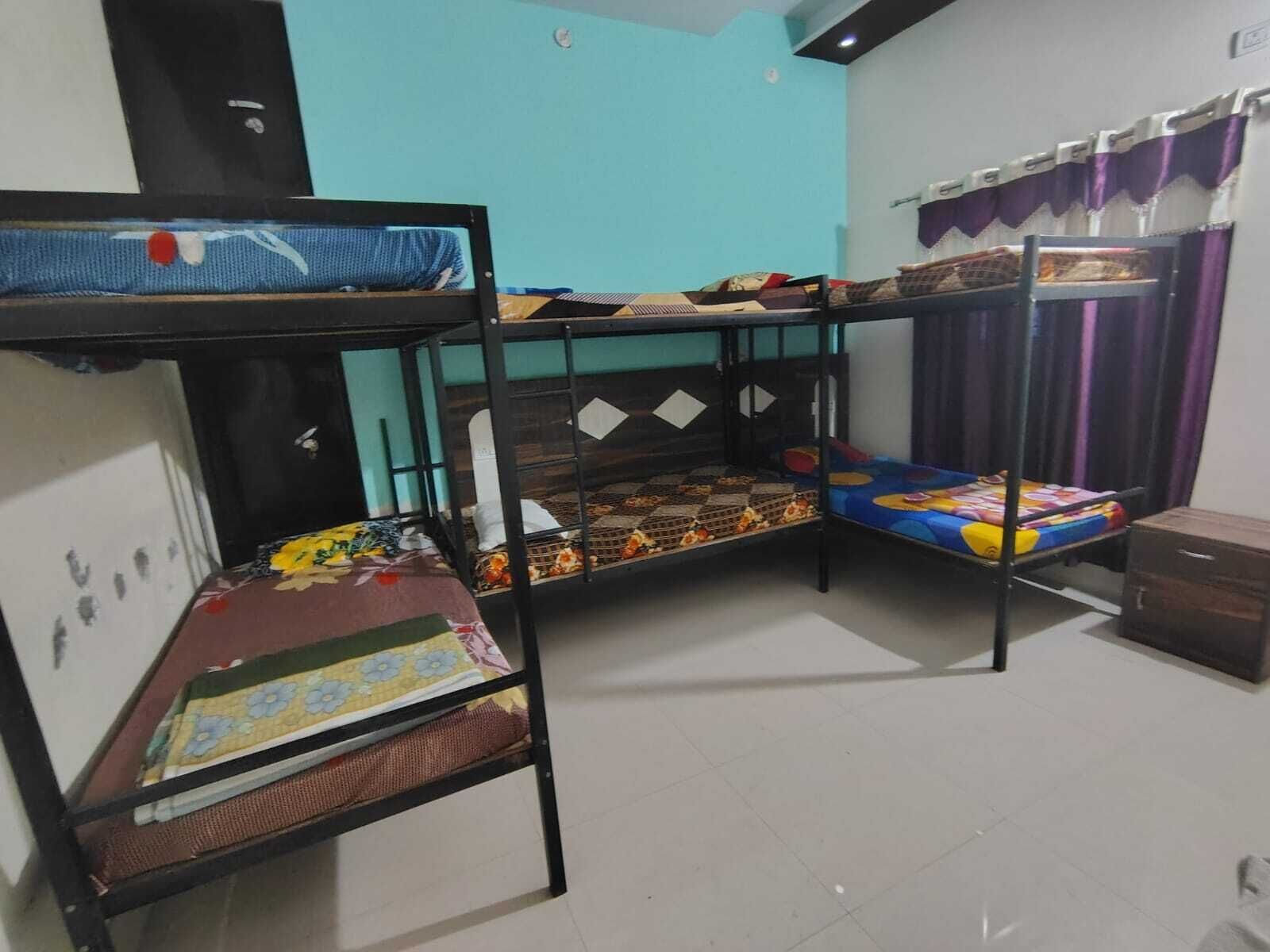 A dormitory room with bunk beds, a small cabinet, and a window with curtains.