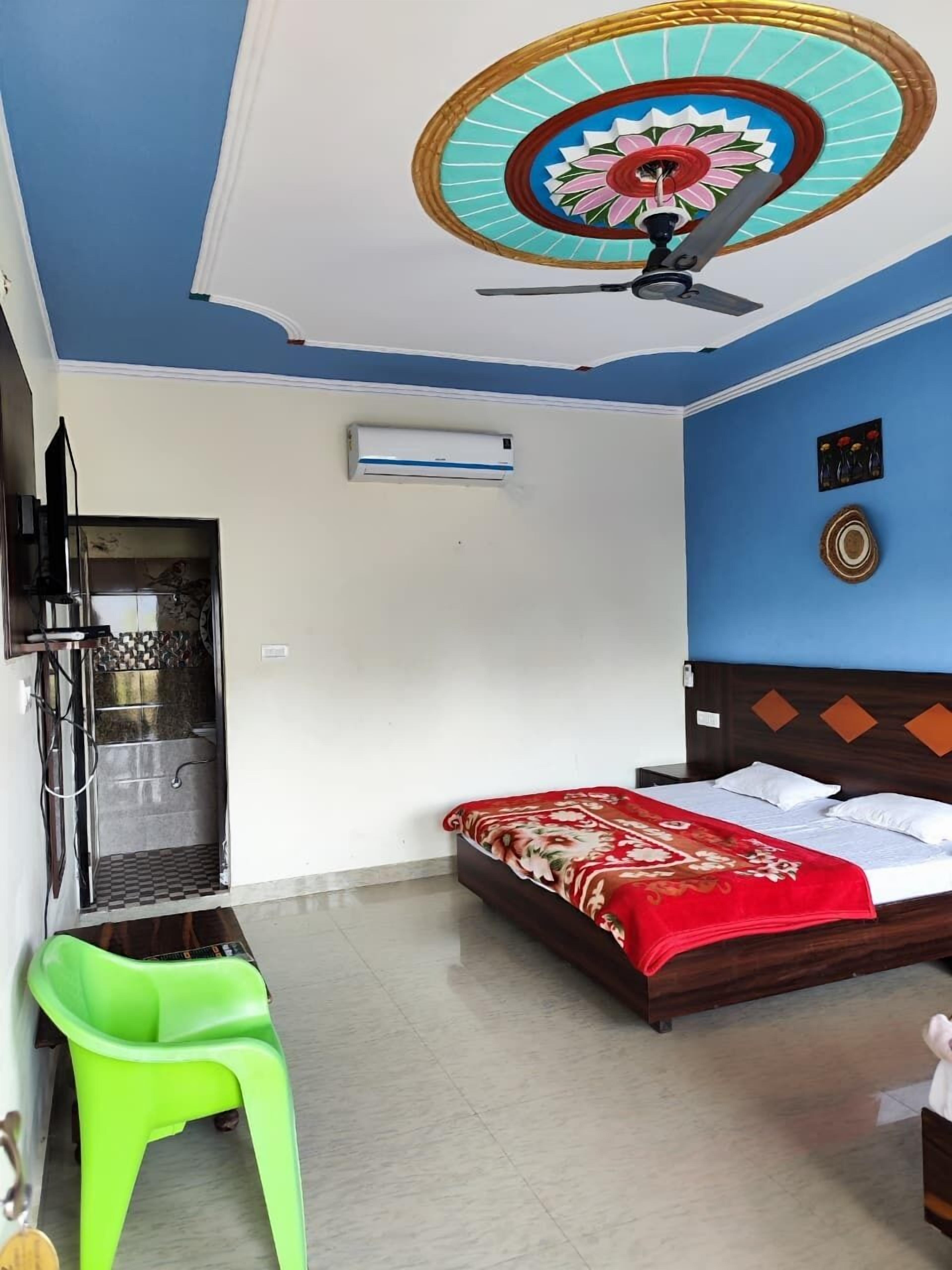 A hotel room with a bed, a ceiling fan, an air conditioning unit, a shower, and a green chair.
