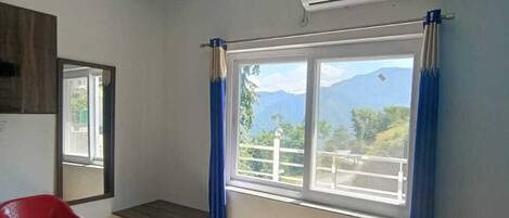 A room with a bed, a red chair, a small table, a ceiling fan, and a window with a view of mountains.