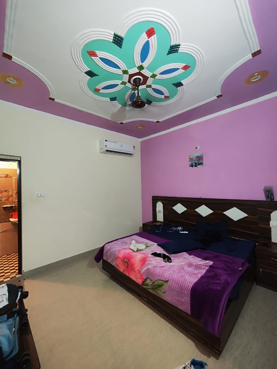 Une chambre à coucher avec un lit, une tête de lit en bois, un ventilateur de plafond et un climatiseur fixé au mur.