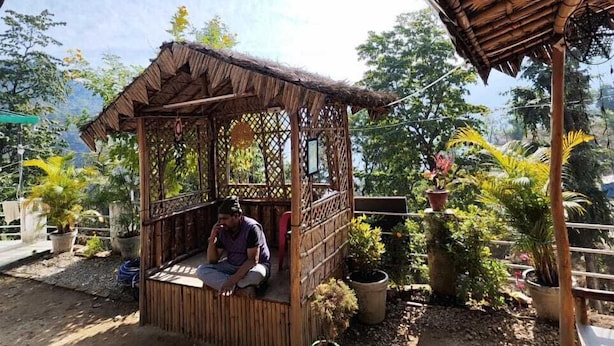 A small bamboo hut with a thatched roof, surrounded by potted plants and trees. - Nature villa Kyarki (Rishikesh)