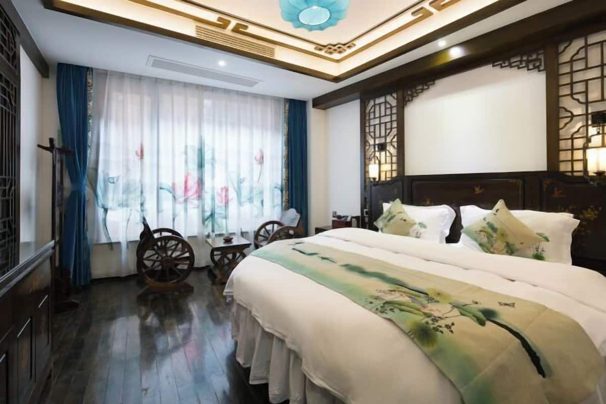 A hotel room with a large bed, a wooden headboard, a traditional Chinese-style window, and a small table with chairs.
