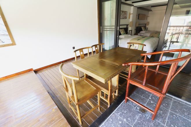 Una habitación con una mesa y sillas de madera, una cama con colcha blanca y una ventana con vistas.