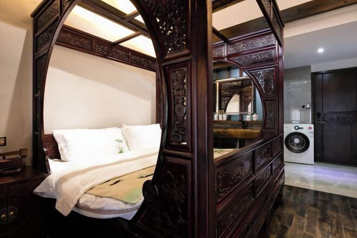 A four-poster bed with intricate carvings, a washing machine, and a dark wooden door.