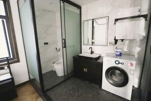 A modern bathroom with a glass shower enclosure, a sink, a mirror, and a washing machine. - Floral Hotel ·Fenghuang Grand Riverview (Fenghuang)