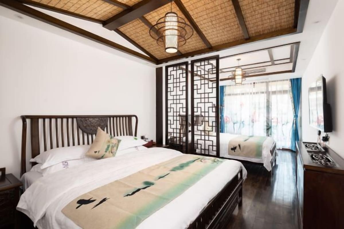 A bedroom with a bed, a nightstand, a wooden headboard, a ceiling fan, a decorative screen, and a television.