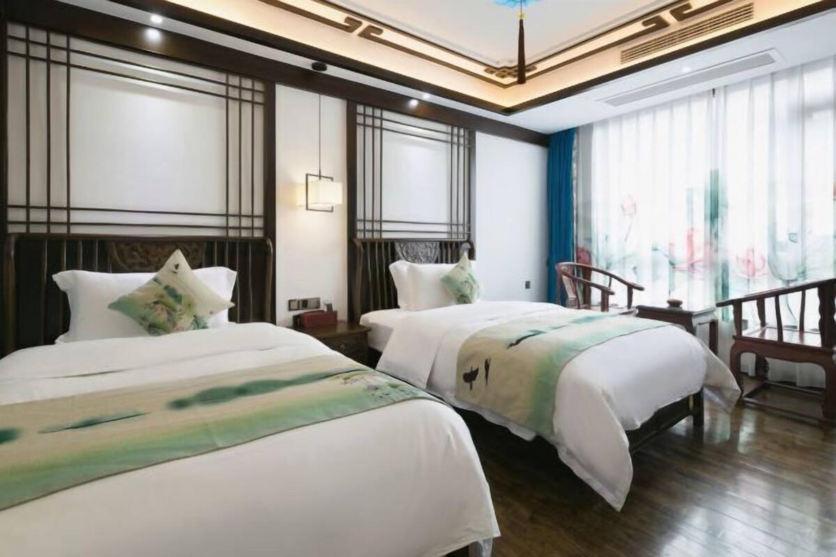 A hotel room with two beds, a wooden floor, a staircase, and a large window with curtains.