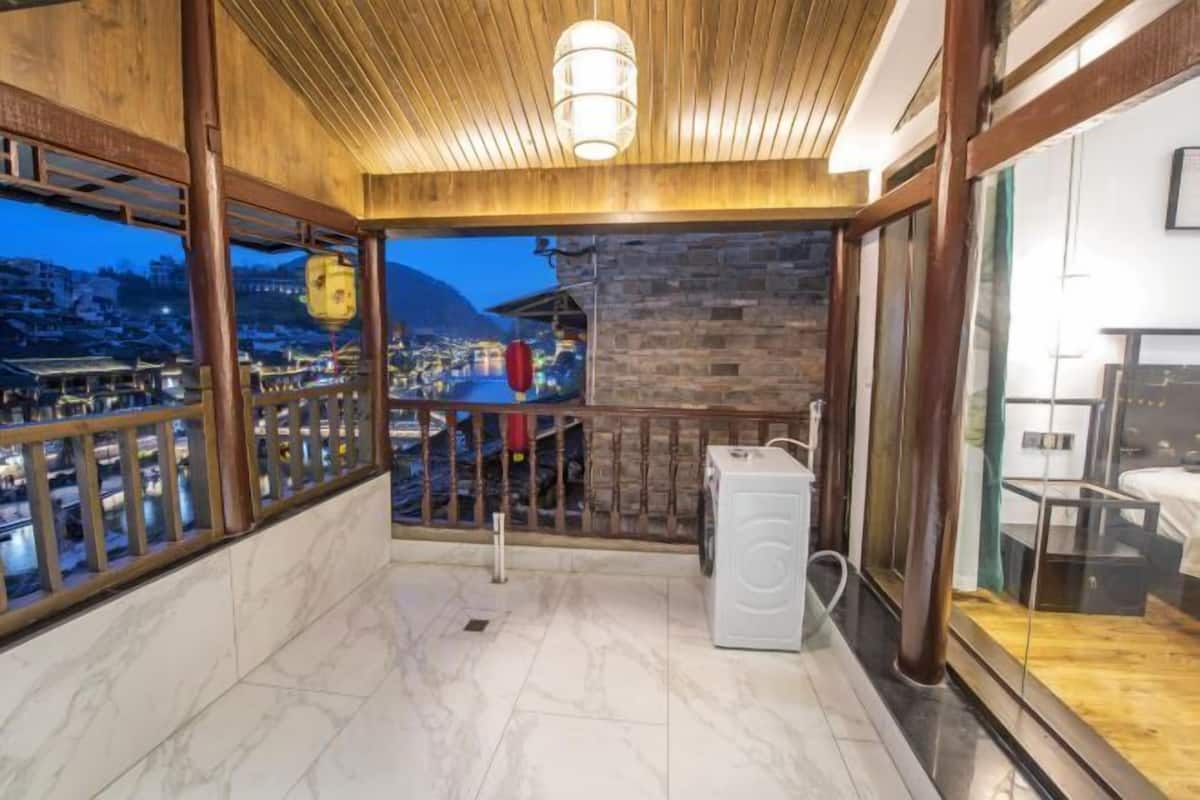 A balcony with a view of a town at dusk, wooden railings, a washing machine, and a stone wall.