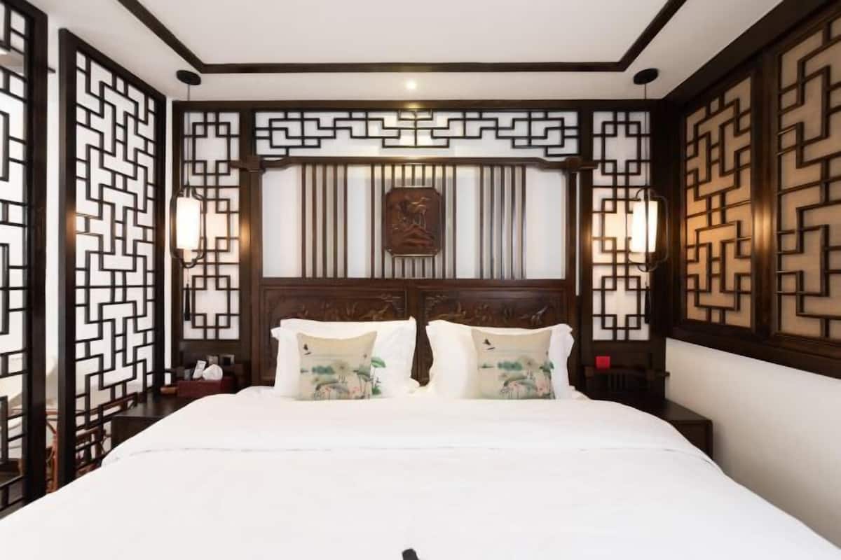 A hotel room with a large bed, decorative wall panels, and two bedside lamps.
