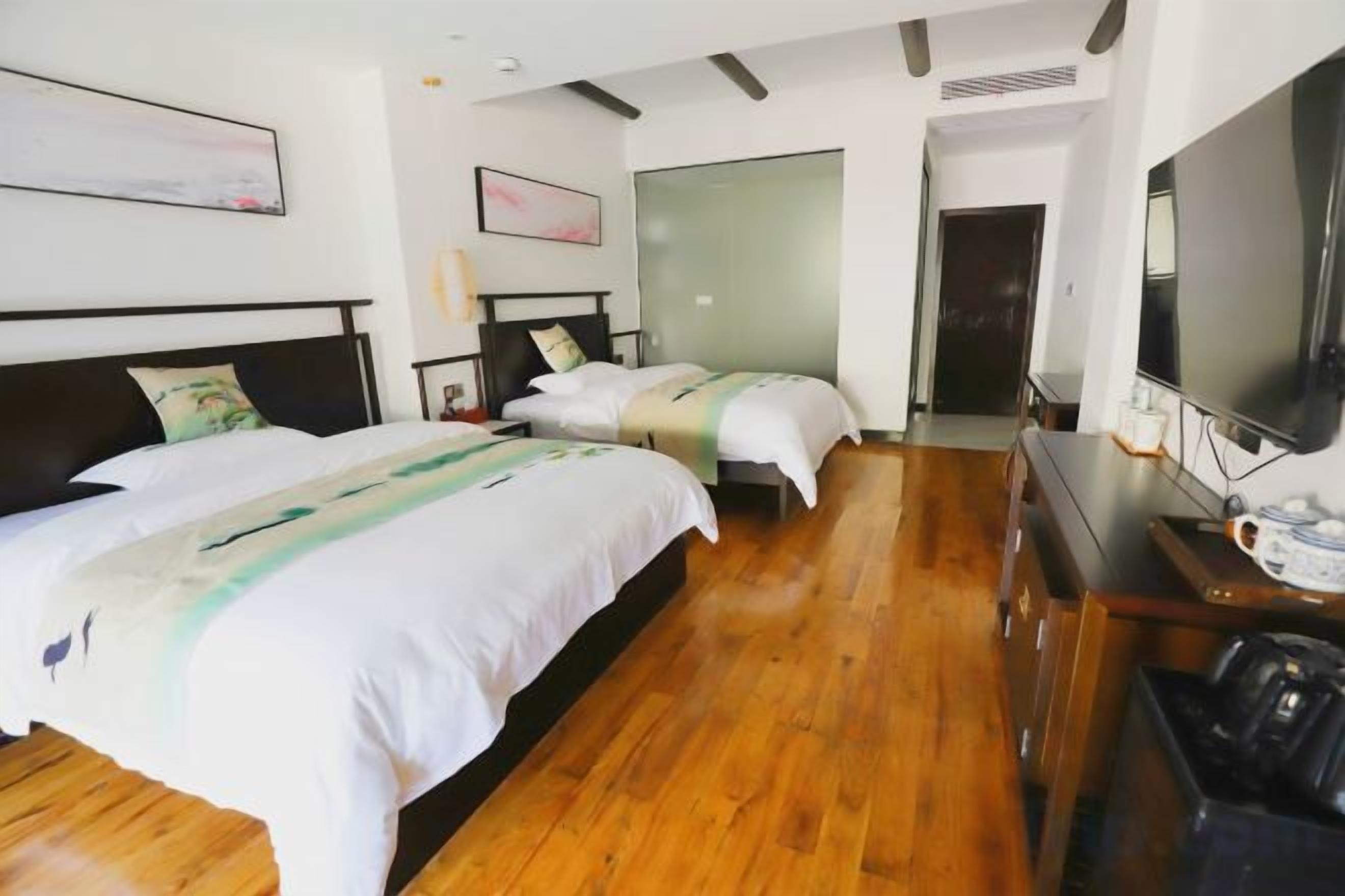 A hotel room with two beds, a television, and a wooden floor.