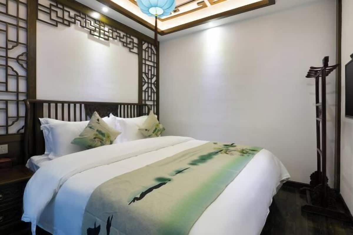 A hotel room with a bed, a decorative wall panel, a ceiling light fixture, and a television on the wall.