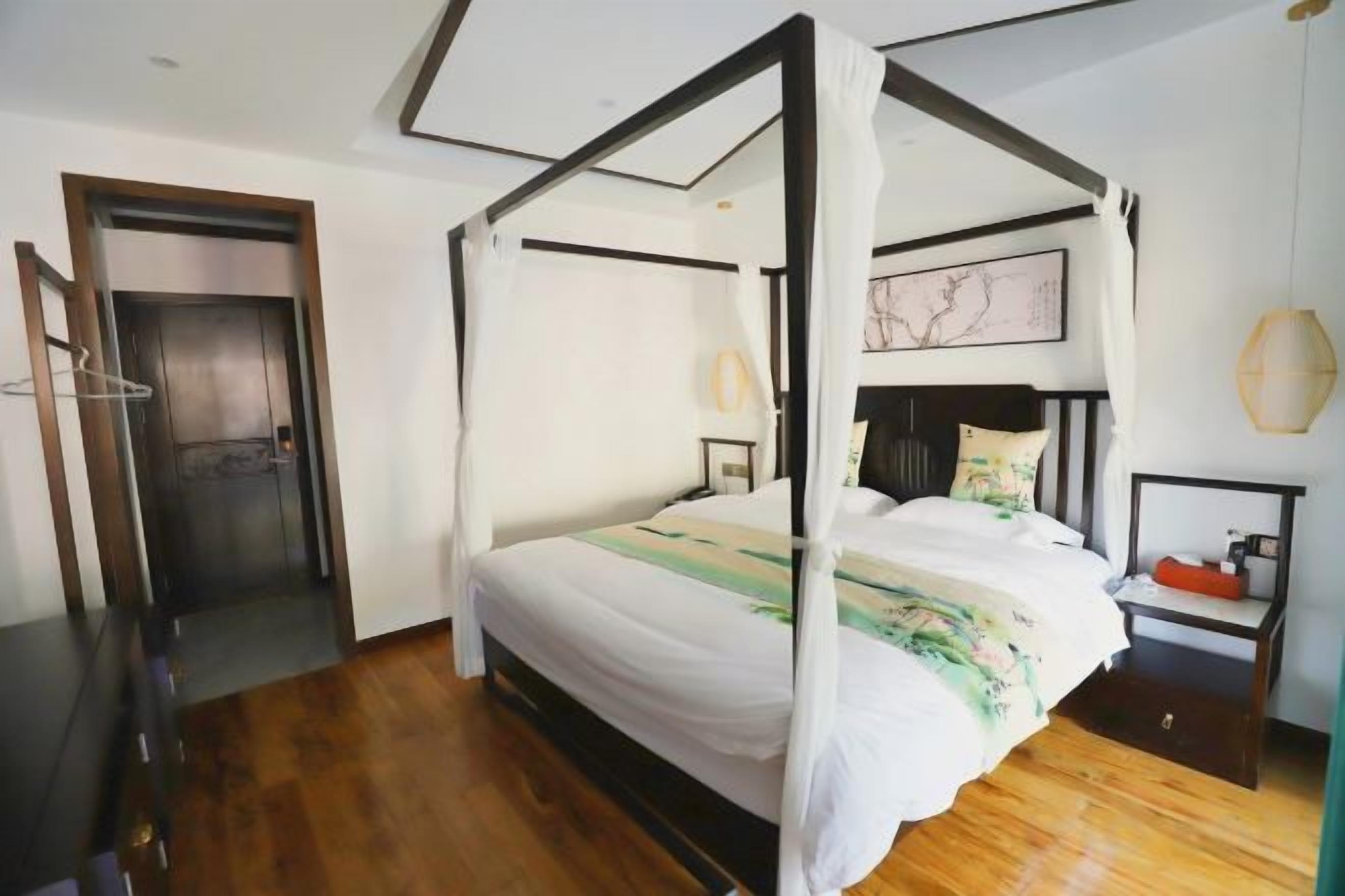 A four-poster bed with a canopy, a bedside table, a nightstand, and a wall-mounted lamp.
