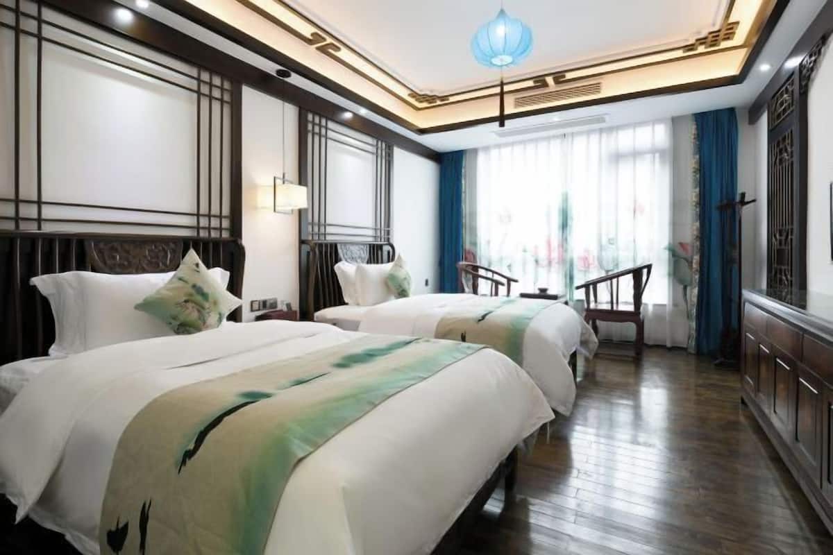 A hotel room with two beds, a wooden floor, a chandelier, and a view of the outside.