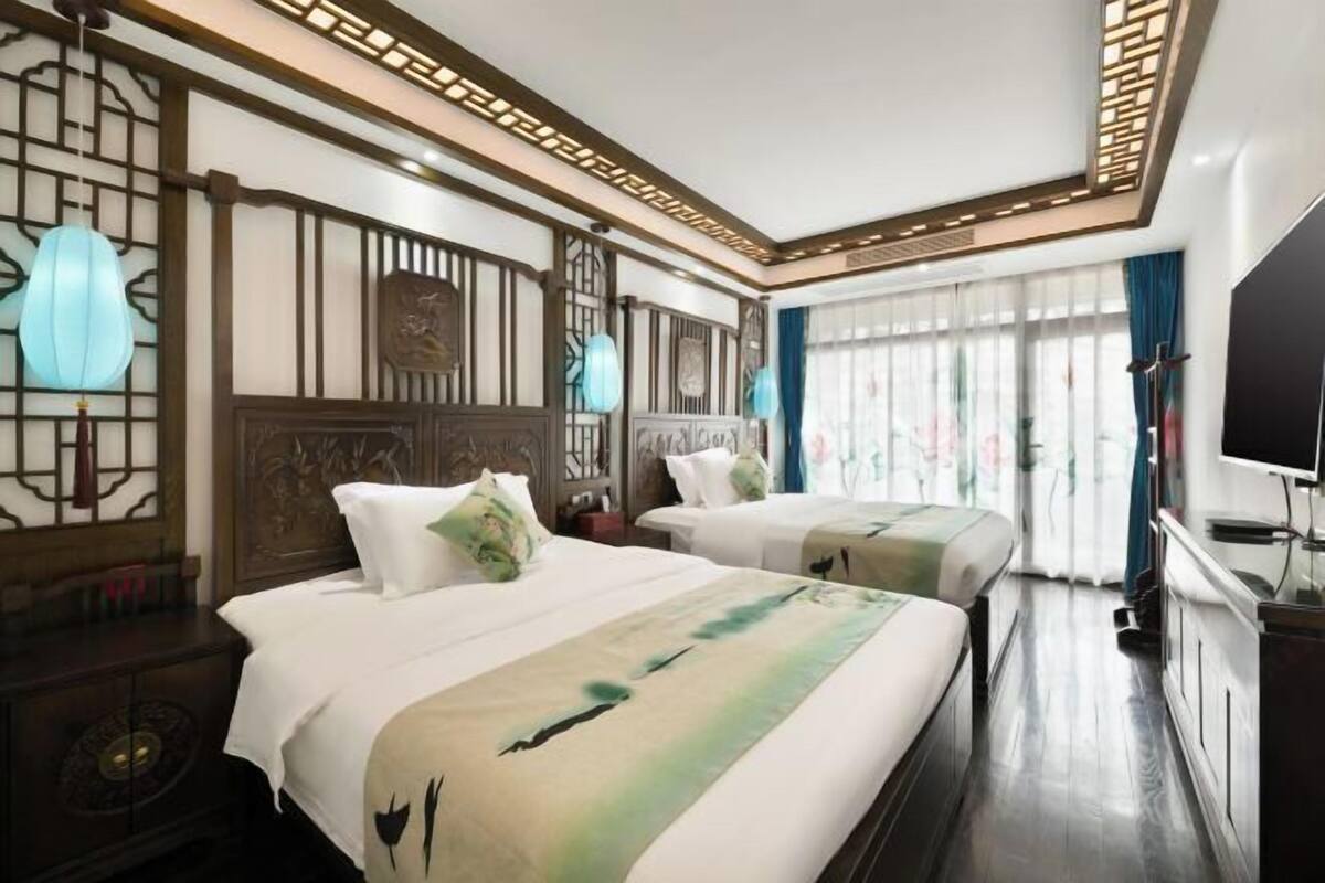 A hotel room with two beds, a TV, and a large window with curtains.
